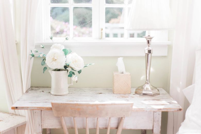 A beige vintage wood desk and chair against a wall, with a lamp and a based with roses - home decor hashtags for Instagram.