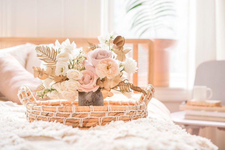 Pale pink and cream-coloured flowers in a vase in a rattan basket on a blanket on a bed - 31 October blog post ideas. 